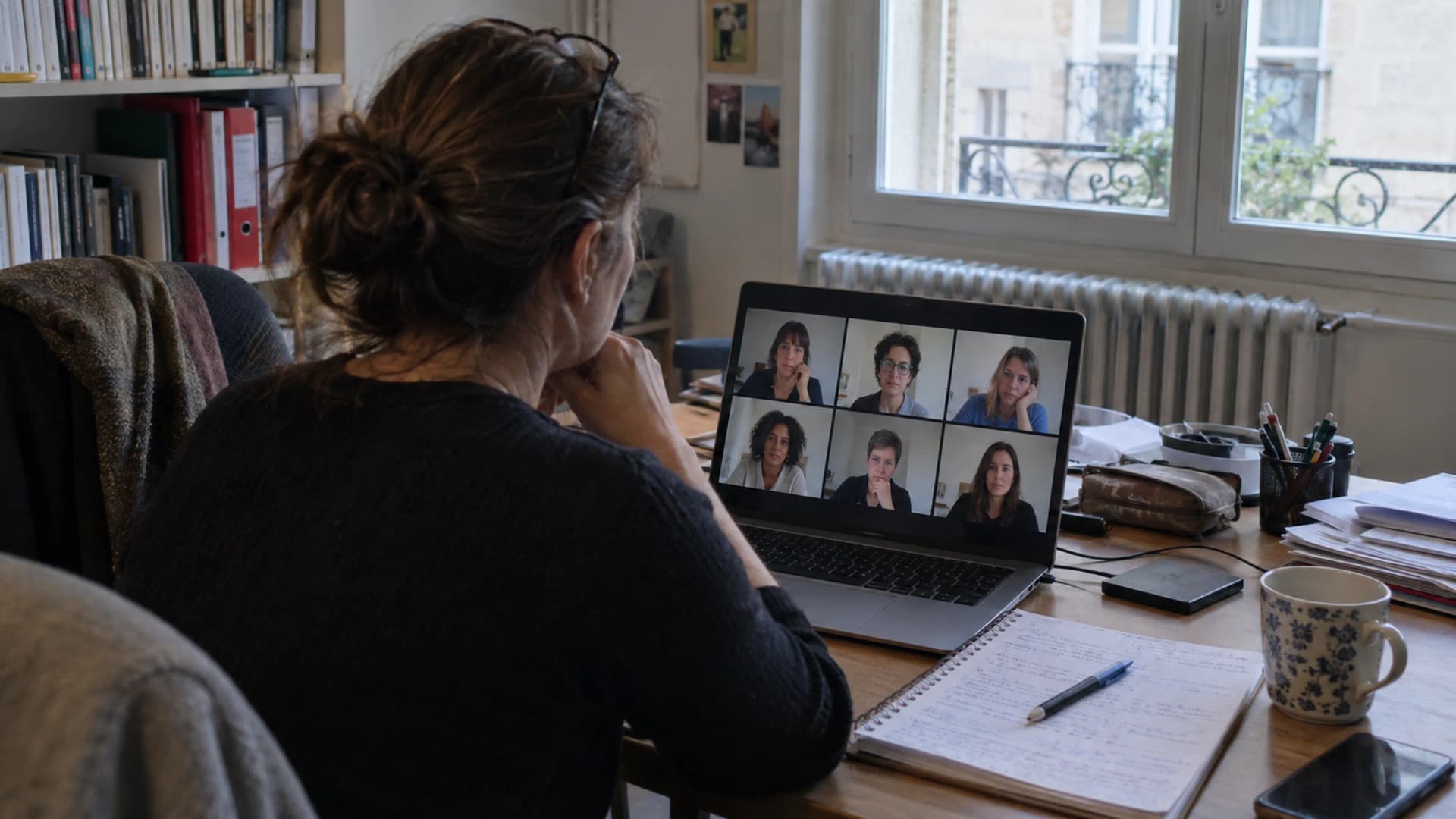 Une psychologue devant son ordinateur portable, le groupe de six participantes visible à l'écran, dans un cabinet lumineux.